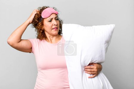 Photo for Pretty middle age woman feeling puzzled and confused, scratching head wearing pajamas night wear and a pillow - Royalty Free Image