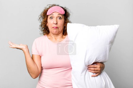 Foto de Mujer de mediana edad bastante desconcertado y confundido y dudando de usar pijamas ropa de noche y una almohada - Imagen libre de derechos