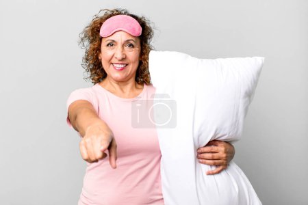 Foto de Mujer de mediana edad bastante apuntando a la cámara eligiéndote usando pijamas ropa de noche y una almohada - Imagen libre de derechos