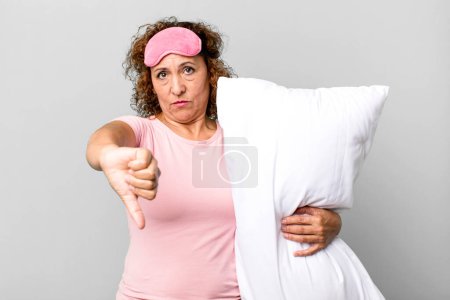 Photo for Pretty middle age woman feeling cross,showing thumbs down wearing pajamas night wear and a pillow - Royalty Free Image