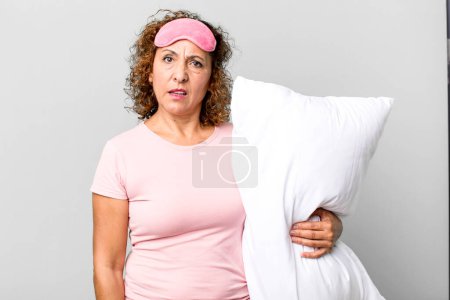 Photo for Pretty middle age woman feeling puzzled and confused wearing pajamas night wear and a pillow - Royalty Free Image