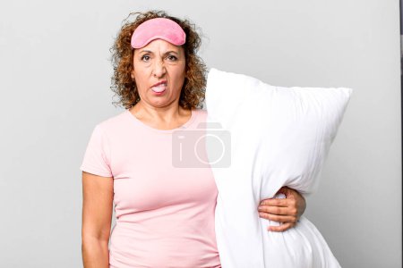 Photo for Pretty middle age woman feeling disgusted and irritated and tongue out wearing pajamas night wear and a pillow - Royalty Free Image