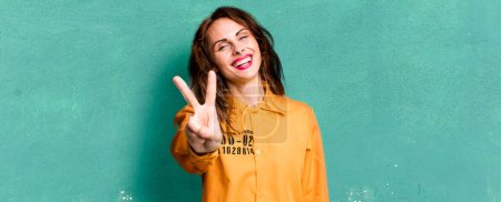 Foto de Hispanic pretty woman smiling and looking happy, gesturing victory or peace. guilt concept - Imagen libre de derechos