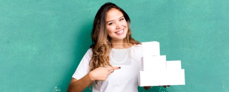 Téléchargez les photos : Hispanic pretty woman smiling cheerfully, feeling happy and pointing to the side with white boxes packages - en image libre de droit