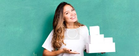 Foto de Mujer bonita hispana sonriendo alegremente, sintiéndose feliz y mostrando un concepto con cajas blancas paquetes - Imagen libre de derechos