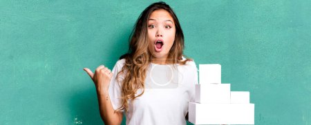 Téléchargez les photos : Hispanique jolie femme regardant étonné dans l'incrédulité avec des boîtes blanches paquets - en image libre de droit
