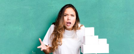 Téléchargez les photos : Hispanique jolie femme à l'air en colère, agacé et frustré par les paquets de boîtes blanches - en image libre de droit