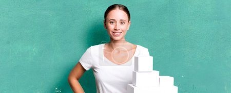 Téléchargez les photos : Caucasian pretty woman smiling happily with a hand on hip and confident with white boxes packages - en image libre de droit