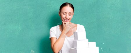 Foto de Caucasian pretty woman smiling with a happy, confident expression with hand on chin with white boxes packages - Imagen libre de derechos