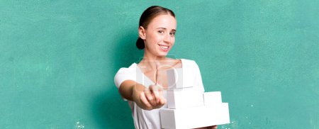 Photo for Caucasian pretty woman smiling proudly and confidently making number one with white boxes packages - Royalty Free Image