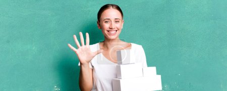 Foto de Caucasian pretty woman smiling and looking friendly, showing number five with white boxes packages - Imagen libre de derechos