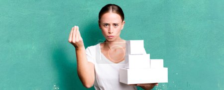 Foto de Caucasian pretty woman making capice or money gesture, telling you to pay with white boxes packages - Imagen libre de derechos