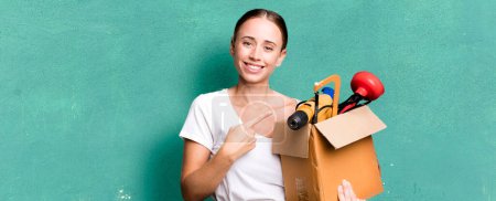Foto de Caucasian pretty woman smiling cheerfully, feeling happy and pointing to the side with a tool box. repair home concept - Imagen libre de derechos