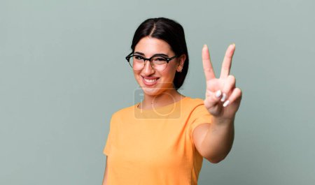 Photo for Smiling and looking happy, carefree and positive, gesturing victory or peace with one hand - Royalty Free Image
