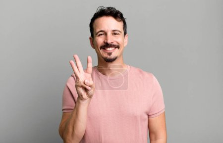 Foto de Sonriendo y mirando amistoso, mostrando el número tres o tercero con la mano hacia adelante, cuenta atrás - Imagen libre de derechos