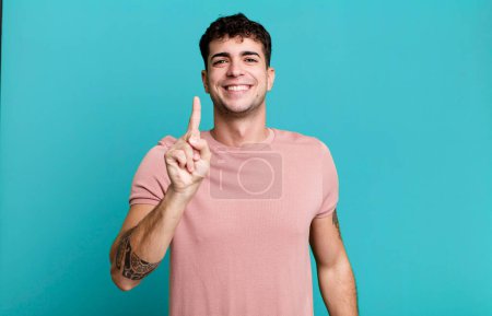 Téléchargez les photos : Homme souriant fièrement et en toute confiance faisant poser le numéro un triomphalement, se sentant comme un leader - en image libre de droit