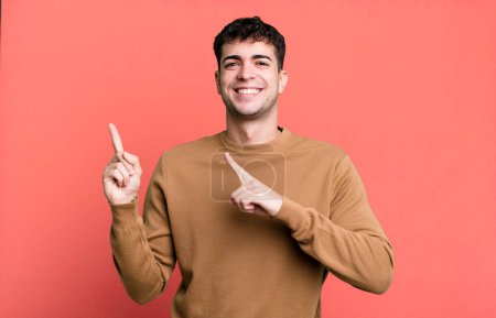 Photo for Man smiling happily and pointing to side and upwards with both hands showing object in copy space - Royalty Free Image