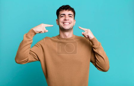 Téléchargez les photos : Homme souriant pointant avec confiance vers son propre sourire large, attitude positive, détendue, satisfaite - en image libre de droit
