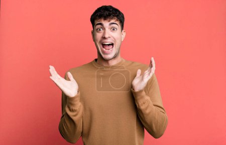 Photo for Man looking happy and excited, shocked with an unexpected surprise with both hands open next to face - Royalty Free Image