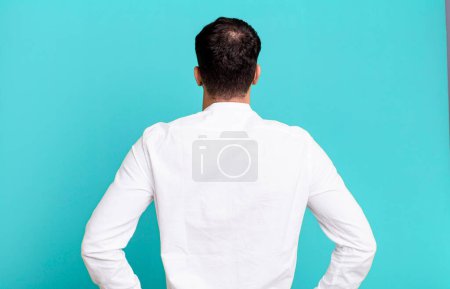 Photo for Man feeling confused or full or doubts and questions, wondering, with hands on hips, rear view - Royalty Free Image