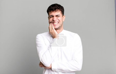 Photo for Man holding cheek and suffering painful toothache, feeling ill, miserable and unhappy, looking for a dentist - Royalty Free Image