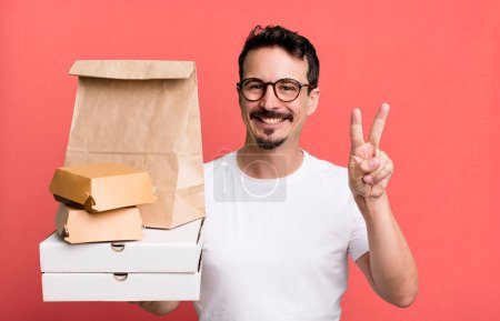 Photo for Adult man smiling and looking happy, gesturing victory or peace. fast food delivery and take away concept - Royalty Free Image