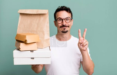 Foto de Adult man smiling and looking friendly, showing number two. fast food delivery and take away concept - Imagen libre de derechos