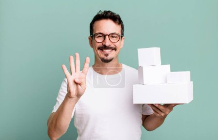 Foto de Adult man smiling and looking friendly, showing number four. blank boxes packaging concept - Imagen libre de derechos
