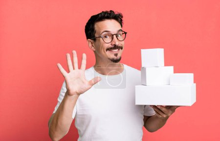 Foto de Adult man smiling and looking friendly, showing number five. blank boxes packaging concept - Imagen libre de derechos
