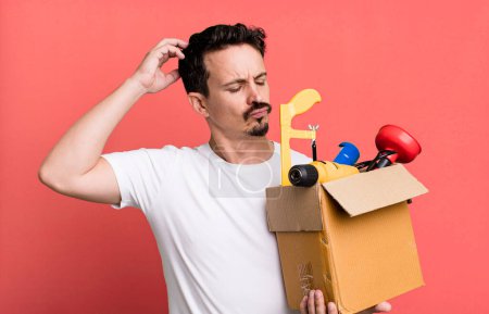 Foto de Adult man feeling puzzled and confused, scratching head. with a toolbox. handyman concept - Imagen libre de derechos