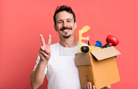 Téléchargez les photos : Adult man smiling and looking happy, gesturing victory or peace. with a toolbox. handyman concept - en image libre de droit