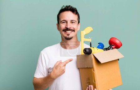 Photo for Adult man smiling cheerfully, feeling happy and pointing to the side. with a toolbox. handyman concept - Royalty Free Image
