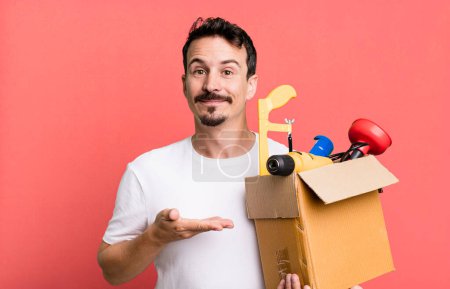 Foto de Adult man smiling cheerfully, feeling happy and showing a concept. with a toolbox. handyman concept - Imagen libre de derechos