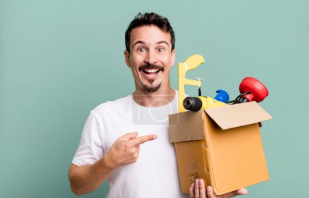 Foto de Adult man looking excited and surprised pointing to the side. with a toolbox. handyman concept - Imagen libre de derechos