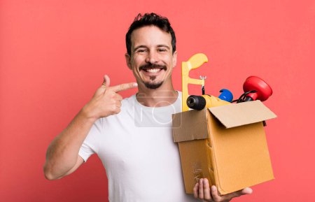 Téléchargez les photos : Adult man smiling confidently pointing to own broad smile. with a toolbox. handyman concept - en image libre de droit
