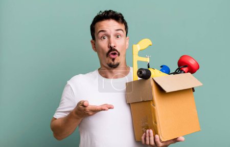 Photo for Adult man looking surprised and shocked, with jaw dropped holding an object. with a toolbox. handyman concept - Royalty Free Image
