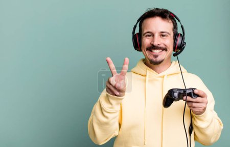Téléchargez les photos : Adult man smiling and looking happy, gesturing victory or peace with headset and a control. gamer concept - en image libre de droit