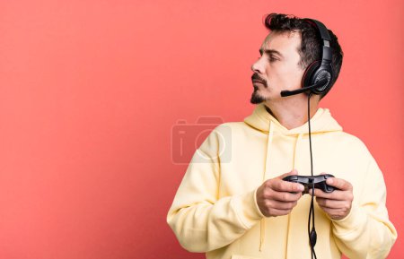 Téléchargez les photos : Adult man on profile view thinking, imagining or daydreaming with headset and a control. gamer concept - en image libre de droit