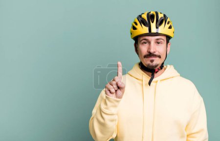 Photo for Adult man smiling and looking friendly, showing number one. bike helmet and bicycle concept - Royalty Free Image