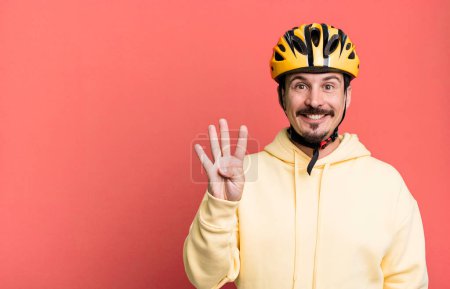 Téléchargez les photos : Adult man smiling and looking friendly, showing number four. bike helmet and bicycle concept - en image libre de droit
