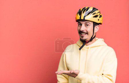 Téléchargez les photos : Adult man smiling cheerfully, feeling happy and showing a concept. bike helmet and bicycle concept - en image libre de droit