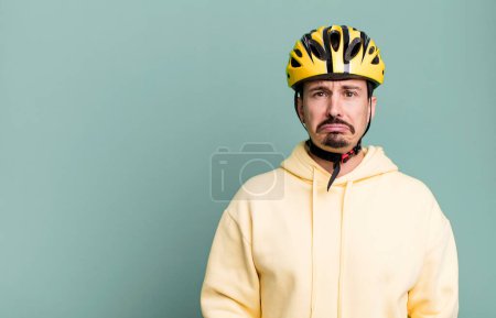Photo for Adult man feeling sad and whiney with an unhappy look and crying. bike helmet and bicycle concept - Royalty Free Image
