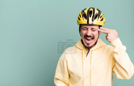 Foto de Adult man looking unhappy and stressed, suicide gesture making gun sign. bike helmet and bicycle concept - Imagen libre de derechos