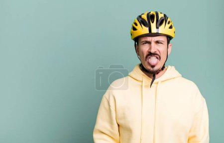 Téléchargez les photos : Adult man feeling disgusted and irritated and tongue out. bike helmet and bicycle concept - en image libre de droit