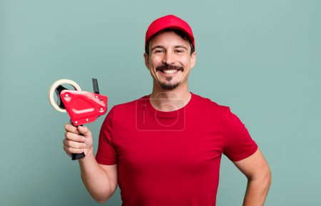 Téléchargez les photos : Adult man smiling happily with a hand on hip and confident. deliveryman packer concept - en image libre de droit