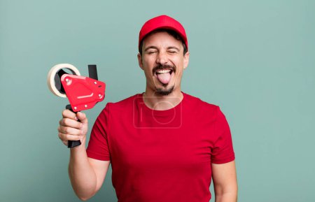 Foto de Adult man with cheerful and rebellious attitude, joking and sticking tongue out. deliveryman packer concept - Imagen libre de derechos