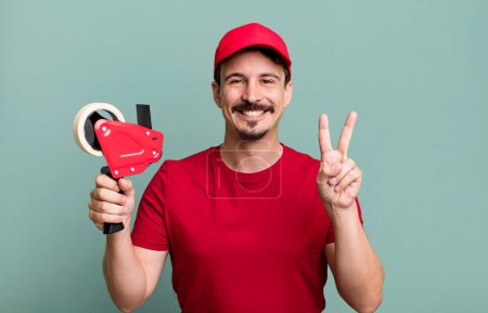 Foto de Adult man smiling and looking friendly, showing number two. deliveryman packer concept - Imagen libre de derechos