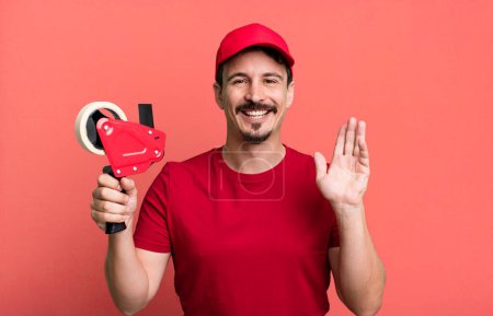 Photo for Adult man smiling happily, waving hand, welcoming and greeting you. deliveryman packer concept - Royalty Free Image