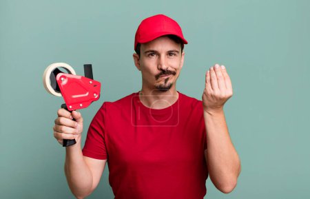 Foto de Adult man making capice or money gesture, telling you to pay. deliveryman packer concept - Imagen libre de derechos