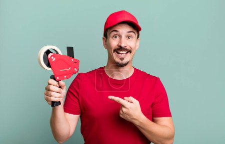 Photo for Adult man looking excited and surprised pointing to the side. deliveryman packer concept - Royalty Free Image